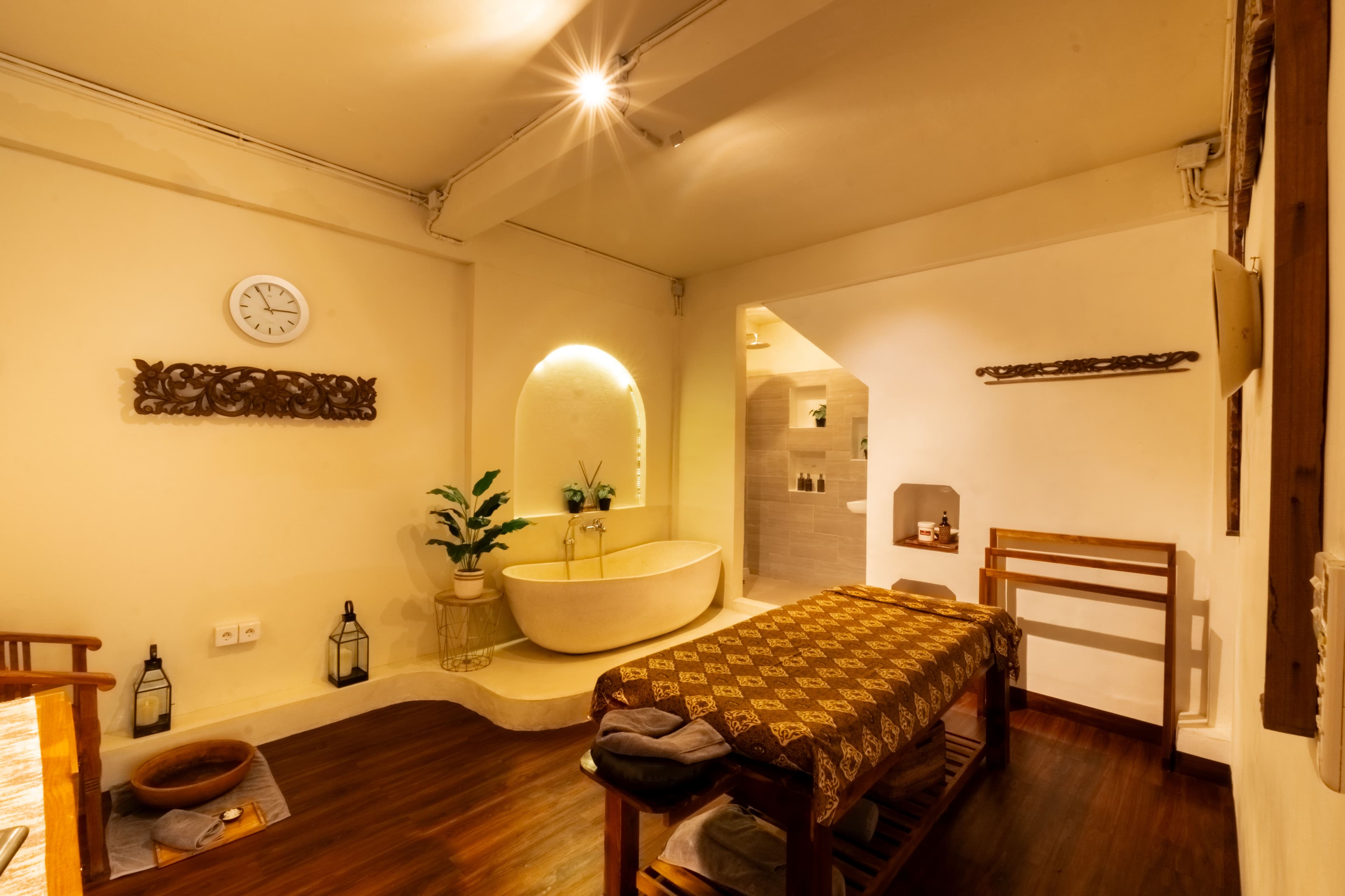 Wide view of a treatment suite with massage bed, bathtub and en-suite shower