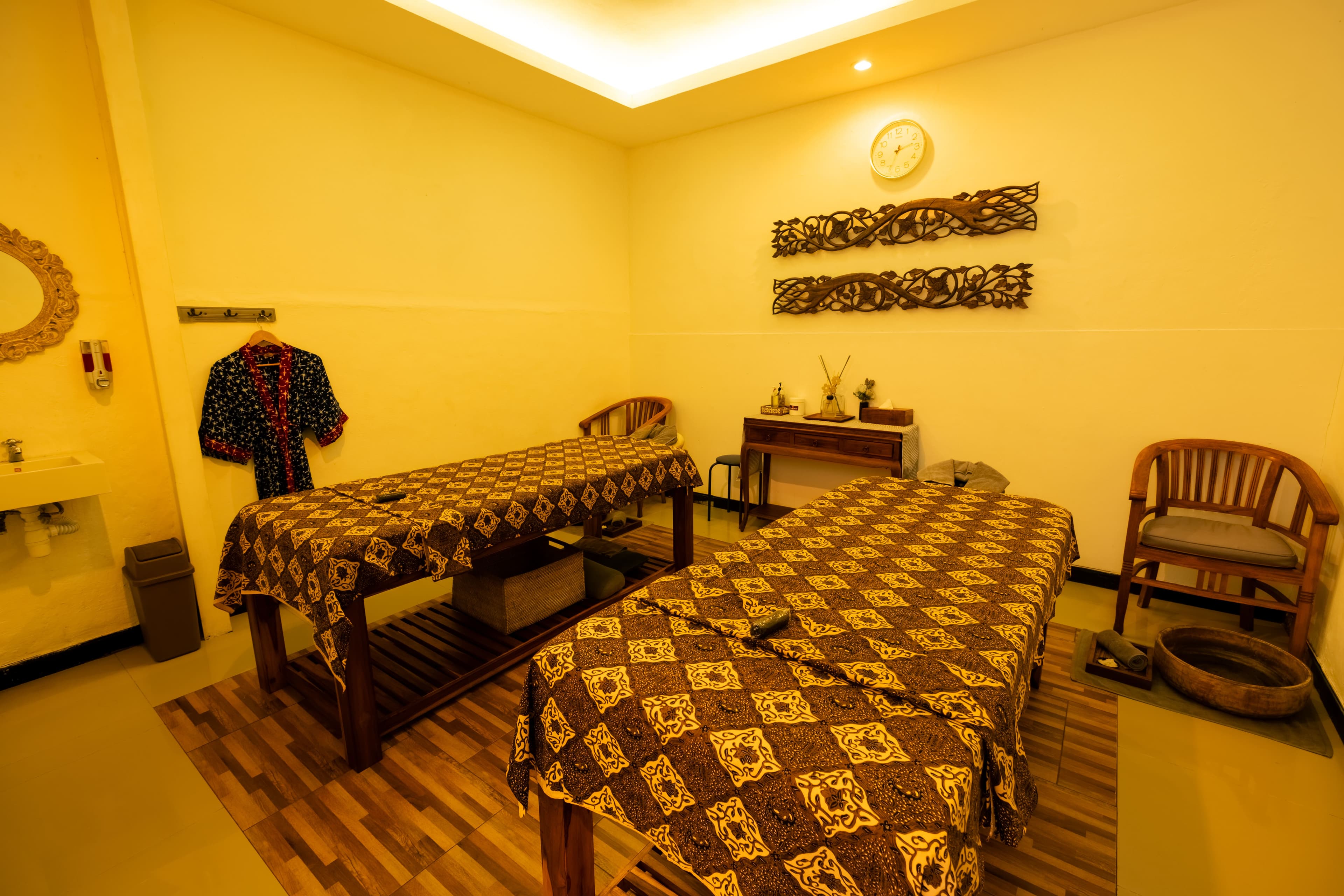 Twin treatment room with two massage beds dressed in batik covers, set up for a couples massage