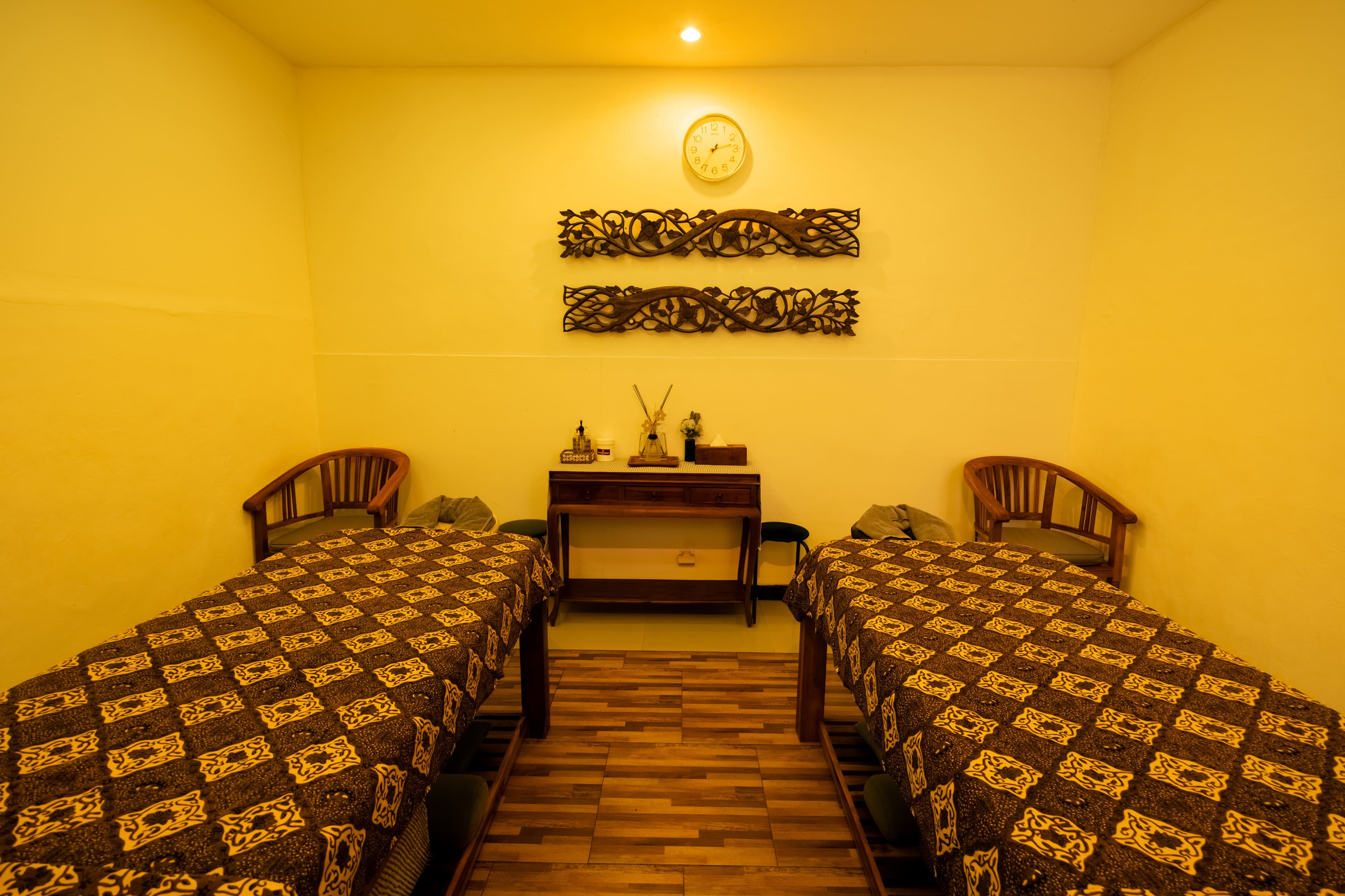 Twin treatment room with massage beds facing a wooden vanity table and carved wall panels