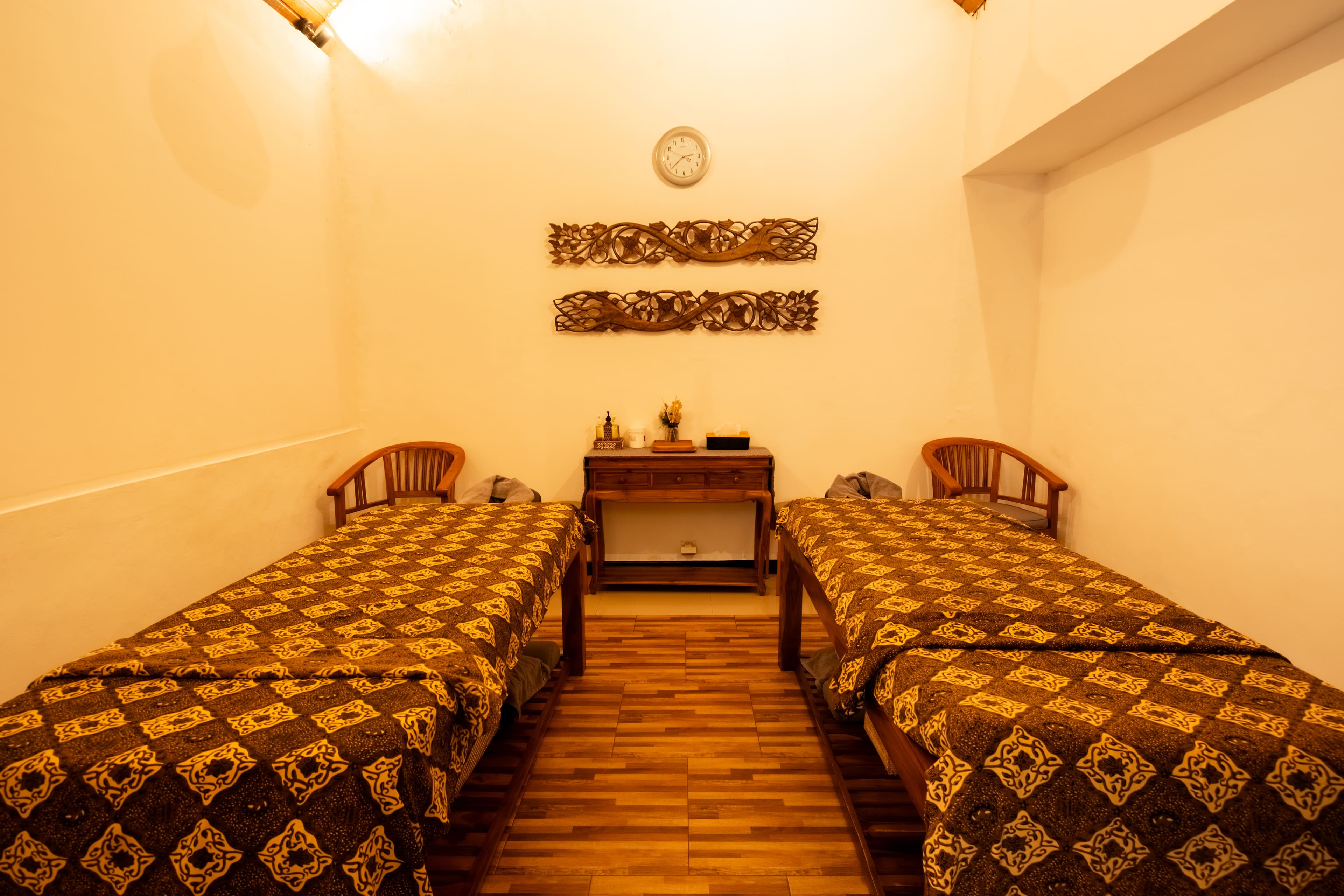 Twin treatment room with matching massage beds and traditional Balinese wood carvings