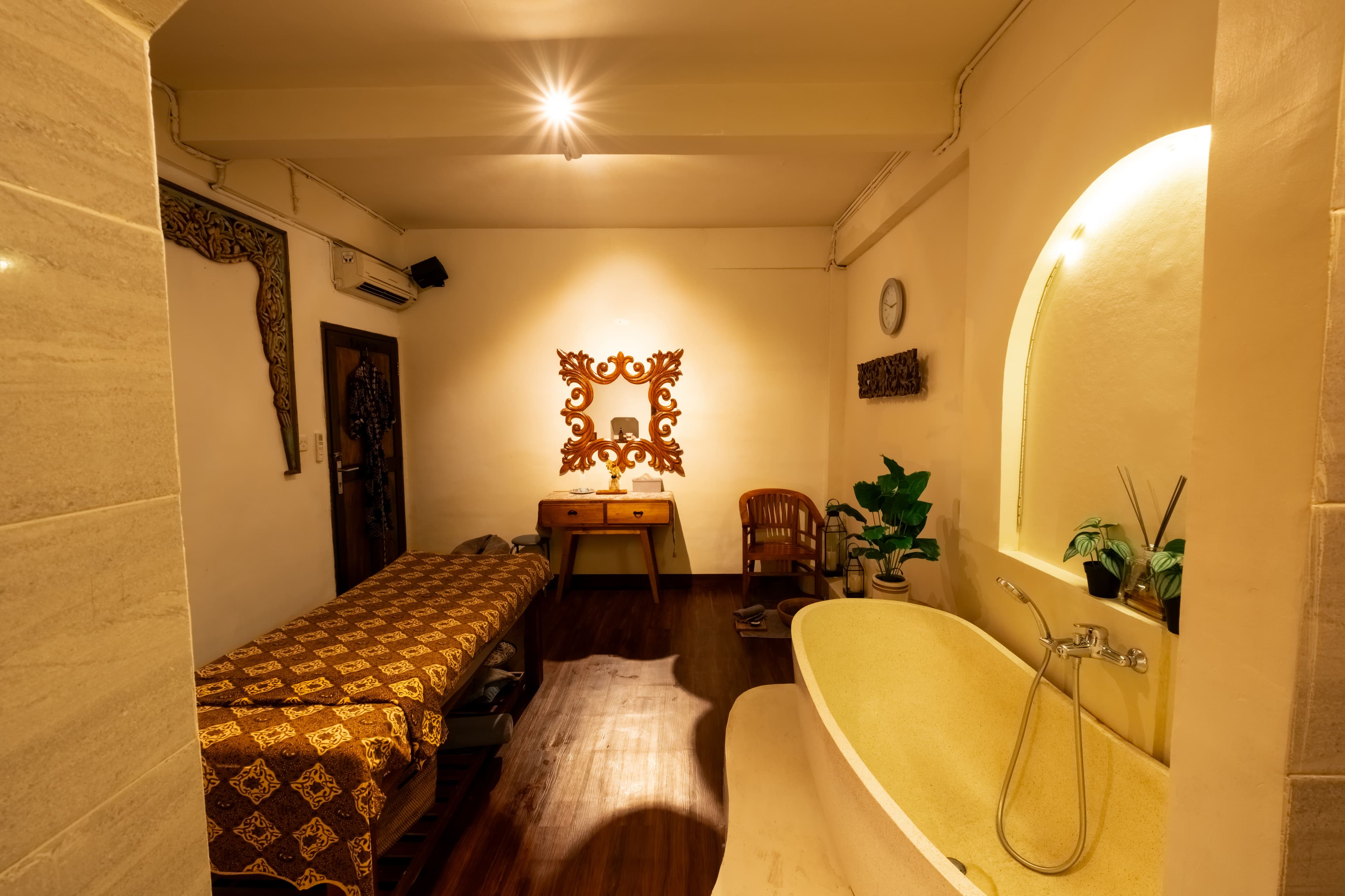 Treatment suite with a massage bed, ornate carved mirror and freestanding bathtub